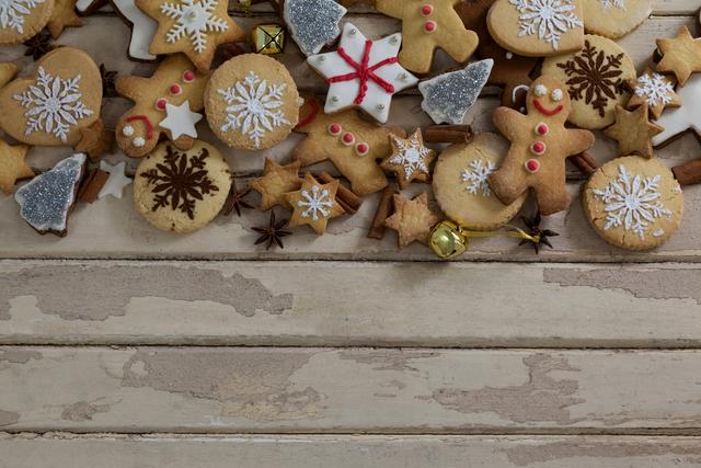 Various types of Christmas cookies arranged on a rustic wooden surface. Includes cookies decorated with snowflakes, gingerbread men, stars, and bells. Ideal for holiday marketing, seasonal promotions, recipe blogs, festive event invitations, and social media posts related to winter celebrations.