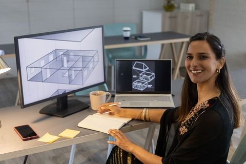 Indian architect designing 3d floor plan at desk with dual monitors, laptop and sketchbook