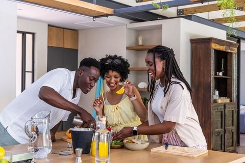 African friends preparing vibrant citrus cocktails and salad at wooden kitchen island in modern home