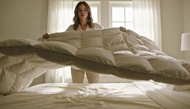 Woman spreading cozy beige duvet over bed in sunlit bedroom for morning routine, home lifestyle