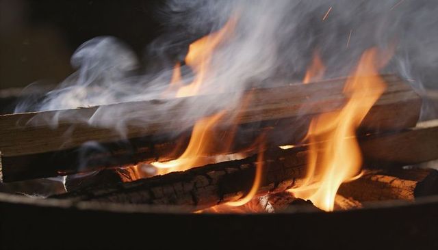 Crackling campfire flames sending smoke over charred logs in backyard firepit close-up