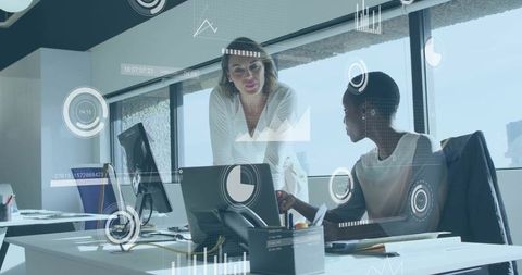 Businesswomen collaborating over laptop with data overlays and HUD charts in modern office
