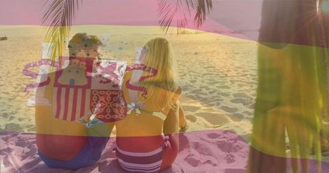 Couple relaxing on sunset beach with spanish flag overlay, tropical palm and golden sand