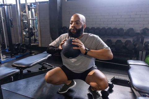 African american man performing medicine ball squat in gym for functional strength training