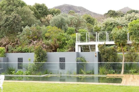 Modern narrow garden pool showing frameless glass fence, timber decking and lush planting