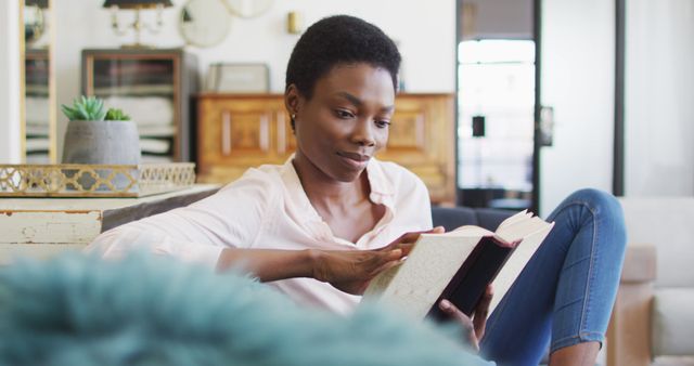 Happy african american woman sitting on sofa in living room, reading book. domestic life, spending time at home.