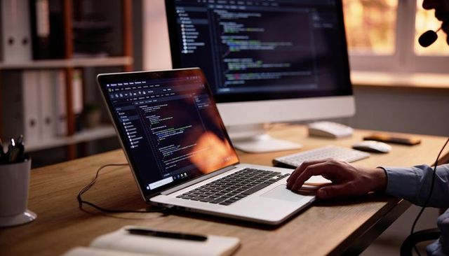 Developer coding on laptop in home office using headset and dual monitors during work