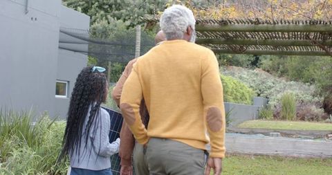 Multigenerational diverse family walking through backyard garden carrying solar panel