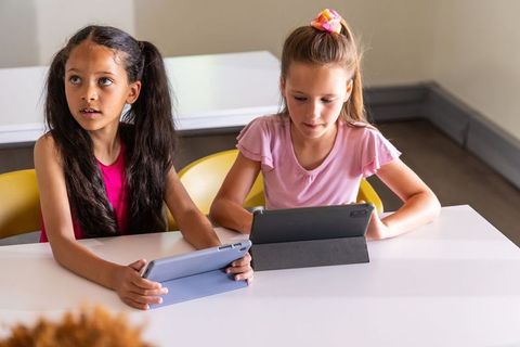 Two schoolgirls using tablets in classroom collaborating on digital learning activities