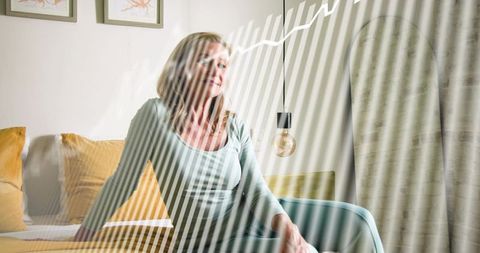 Serene mature blonde woman sitting on bed with striped sunlight and minimalist decor