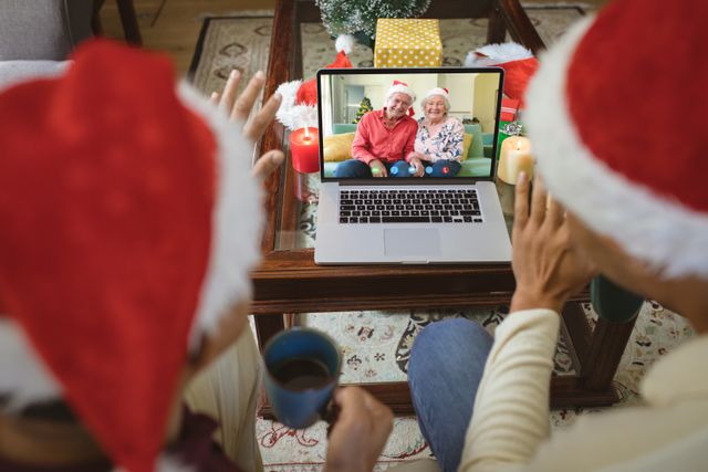 Couple wearing Santa hats is video calling senior family members on a laptop. It represents festive season bonding and maintaining connections even while being remote. Useful for holiday greeting cards, articles on family and technology, and festive season advertisements.