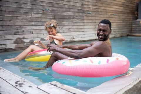 Friends relaxing on colorful floats in private pool enjoying drinks and summer fun