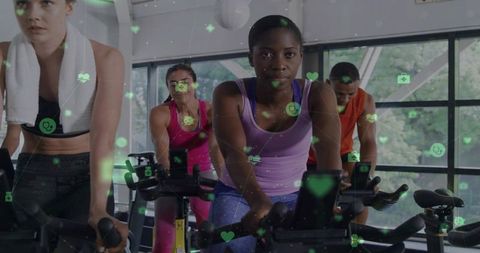 Focused Black Woman Pedaling Indoor Cycling Bike in Group Class with Fitness Consoles