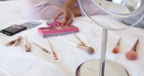 Woman reaching for rose-gold eyeshadow palette on plush towel with makeup brushes