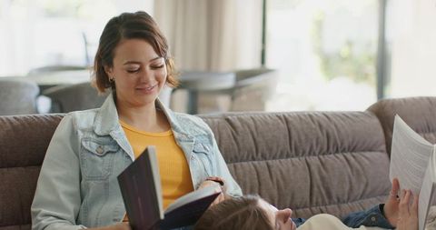 Two women relaxing and reading on tufted sofa in sunlit living room