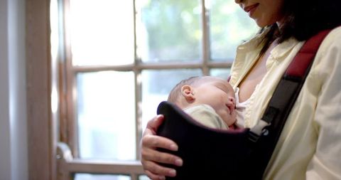 Mother cradling newborn in baby carrier at home