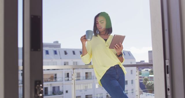 Woman enjoying coffee while reading on tablet on apartment balcony - Download Free Stock Images Pikwizard.com