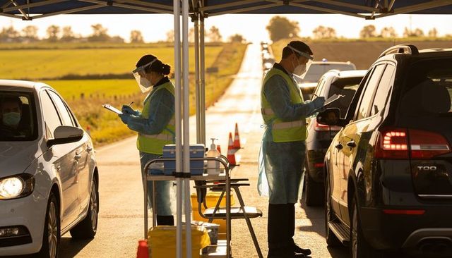 Healthcare workers wearing ppe conducting drive-thru testing at rural roadside checkpoint