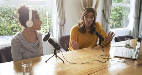 Female co-hosts recording home podcast with microphones, headphones and laptop