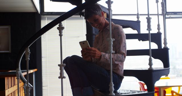 Man sitting on spiral staircase smiling while using smartphone - Download Free Stock Images Pikwizard.com