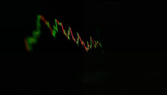 Glowing candlestick chart sloping downward over dark trading desk with laptop reflections