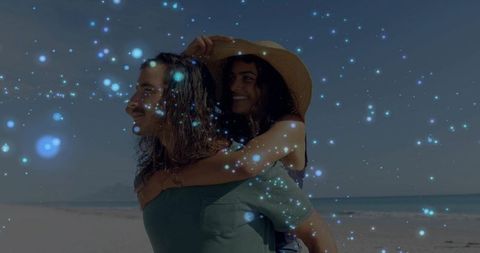 Couple enjoying piggyback ride on sunny beach with straw hat and blue bokeh lights