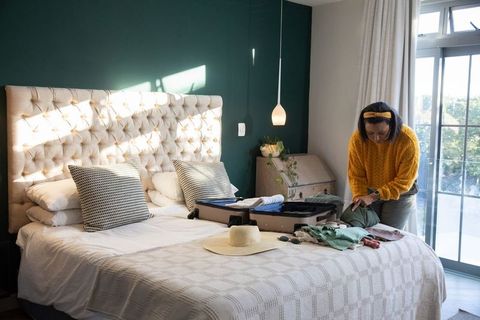 Mature woman packing suitcase in sunlit bedroom preparing for trip