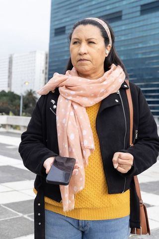Walking city commuter holding smartphone wearing peach polka-dot scarf and mustard sweater