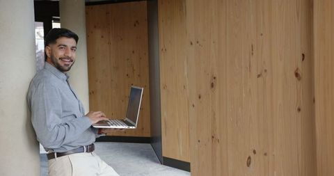 Confident Professional Typing on Laptop in Modern Office Hallway