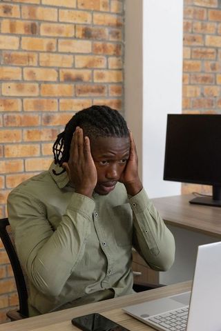 Stressed businessman holding head at laptop in office