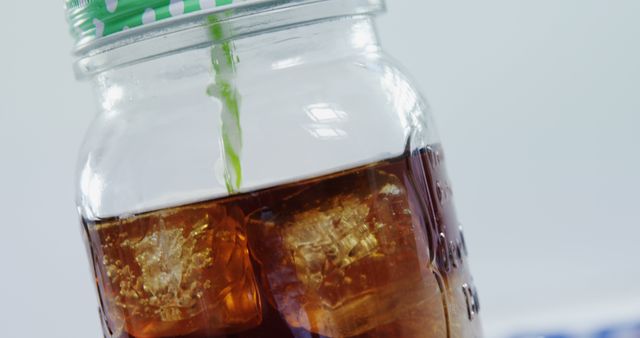 A close-up view of a jar with a green straw, filled with iced tea and ice cubes, with copy space. It captures a refreshing beverage, ideal for quenching thirst on a warm day.