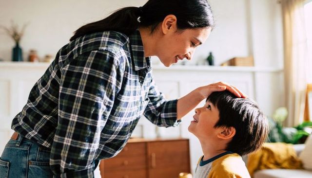 Mother touching son's head and smiling in sunlit living room showing tender family moment