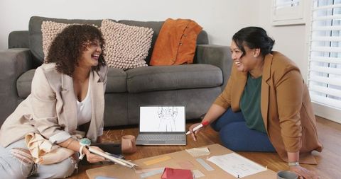 Diverse women collaborating on fashion moodboard with fabric swatches and sketches at home