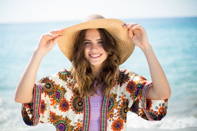 Portrait of happy young woman wearing hat while standing at beach