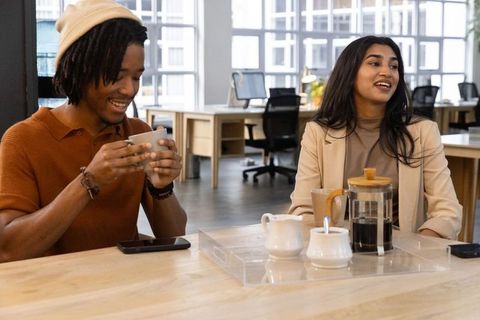 Diverse coworkers sharing coffee and conversation in modern open-plan office