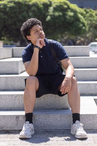 Young man sitting on urban steps contemplating while wearing backpack and fitness tracker