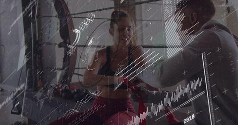 Female boxer preparing for training while coach wrapping hands in boxing ring with data overlay