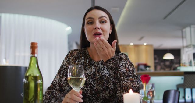 Caucasian woman having romantic dinner at restaurant holding wine glass and blowing kiss to camera. romantic evening out celebrating valentine's day.