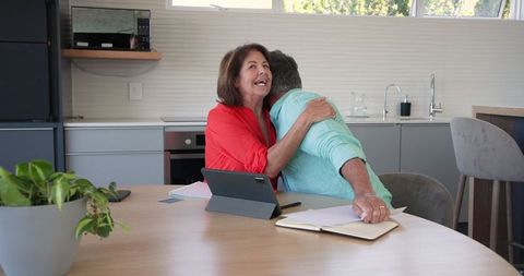 Senior Couple Embracing and Discussing Documents with Tablet