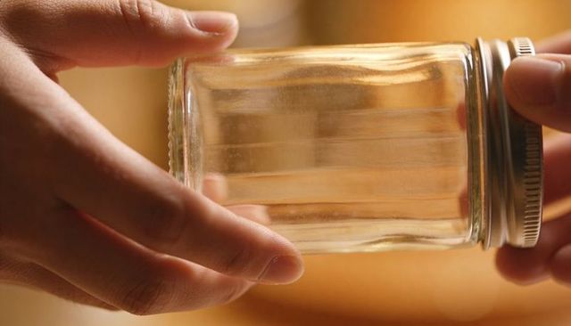 Cradling hands holding empty glass jar with metal screw lid warm amber bokeh background