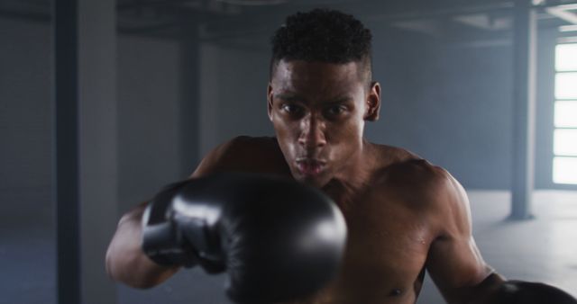 African-American boxer throwing punches in urban gym environment. Ideal for topics related to boxing training, fitness motivation, sports focus, and athletic dedication. Can be used in sports gear advertisements, fitness tutorial materials, or motivational fitness branding.