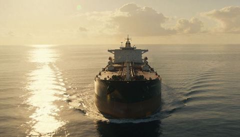 Massive oil tanker sailing into golden sunrise showing deck piping and bow wake aerial view