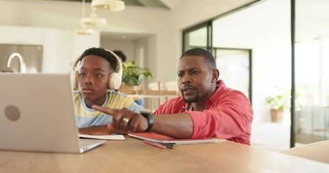 African american father guiding son during online learning at dining table with laptop