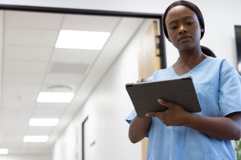 Nurse using tablet in bright modern hospital corridor documenting electronic records
