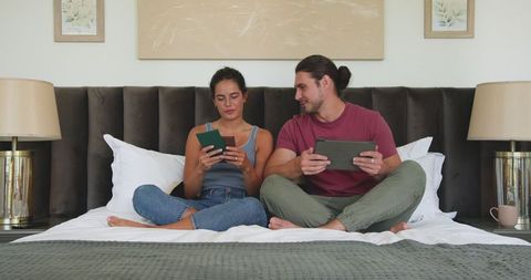 Couple relaxing on bed using tablets for leisure time together
