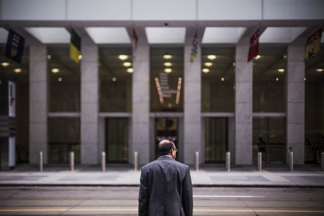 Businessman standing outside a modern office building in a city. The image can be used in corporate presentations, business articles, and advertisements targeting professionals or business-related services.
