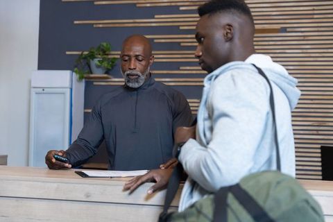 African american hotel clerk checking guest device at modern wooden reception desk