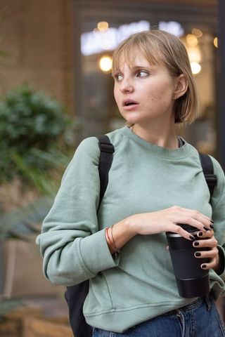 Young urban commuter holding travel mug outside cafe looking left lifestyle portrait