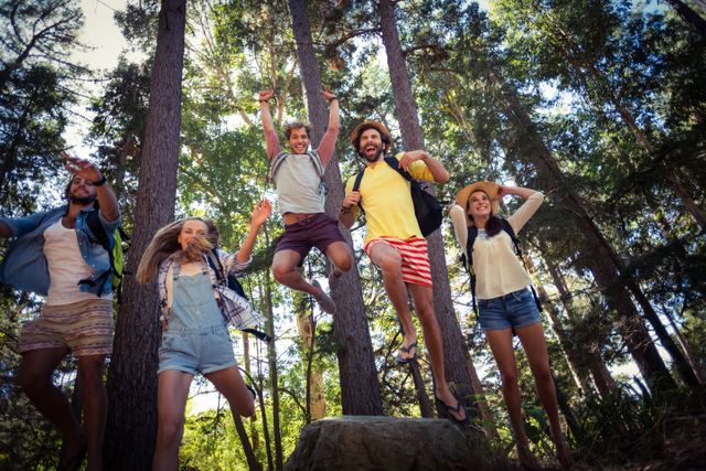 Group of friends jumping and having fun in a forest on a sunny day. Perfect for promoting outdoor activities, travel adventures, youth engagement, and nature exploration. Ideal for use in advertisements, social media campaigns, and travel blogs.