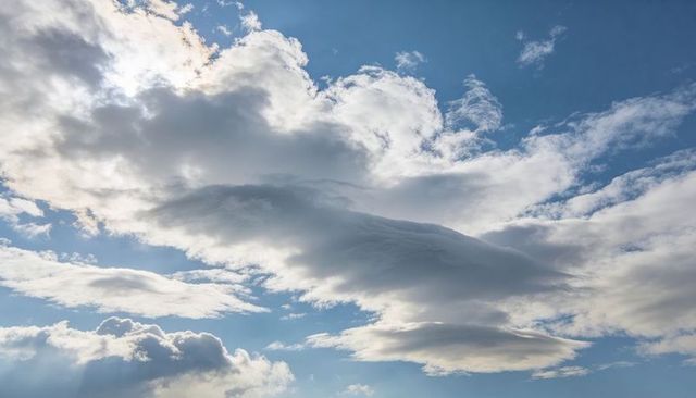 Layered lenticular clouds stretching across sunlit blue sky with dramatic light rays